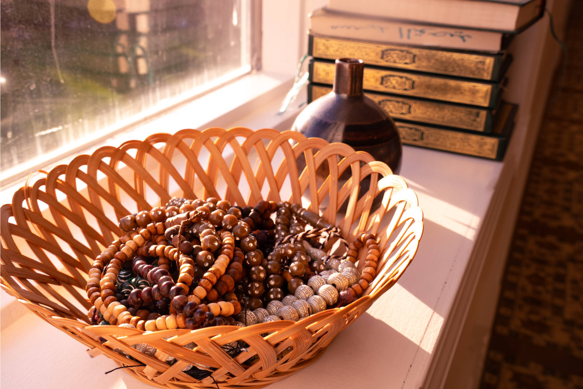 A woven bowl filled with various prayer beads with books in the background.